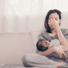 image of a woman holding a baby looking stressed, suffering from PPD